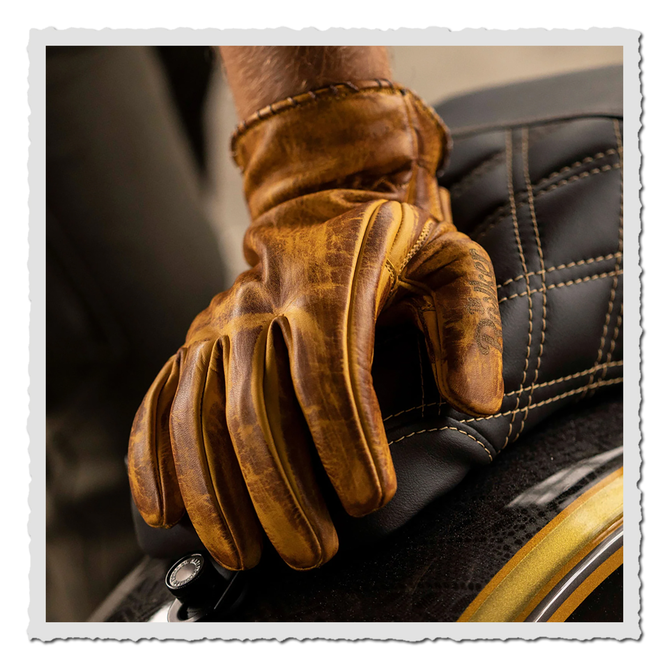 Gelber Leder-Motorradhandschuh am Motorrad, Nahaufnahme auf Sitz mit Steppnähten, warmes Licht, unscharfer Hintergrund.